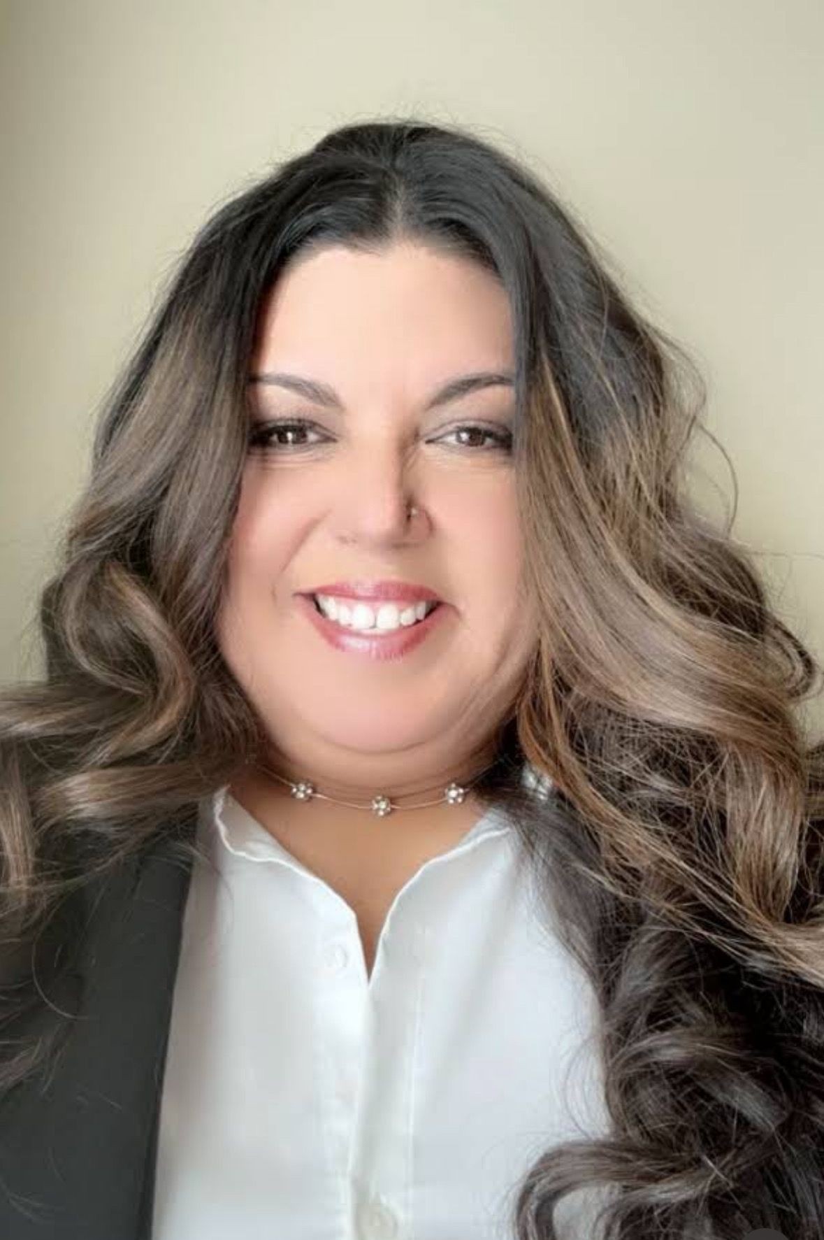 Smiling person with long, wavy hair wearing a white shirt and black jacket.